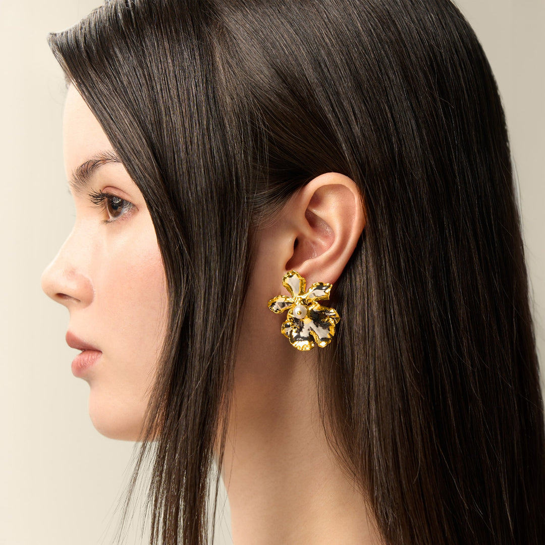 Risis 1974 Oncidium Earrings - A large gold-finish earring, shaped like a flower with intricate petals and a pearl center, adorns a woman's ear.