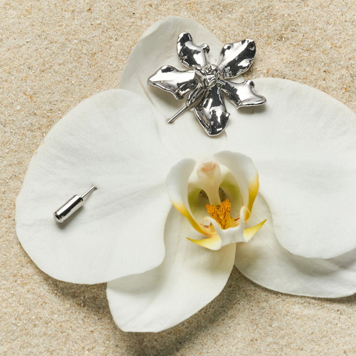 Risis Vanda Limbata Lapel Pin Pd - A shiny silver orchid-shaped brooch with detailed petals and a lifelike center on a real orchid flower, contrasting metallic finish with organic beauty.