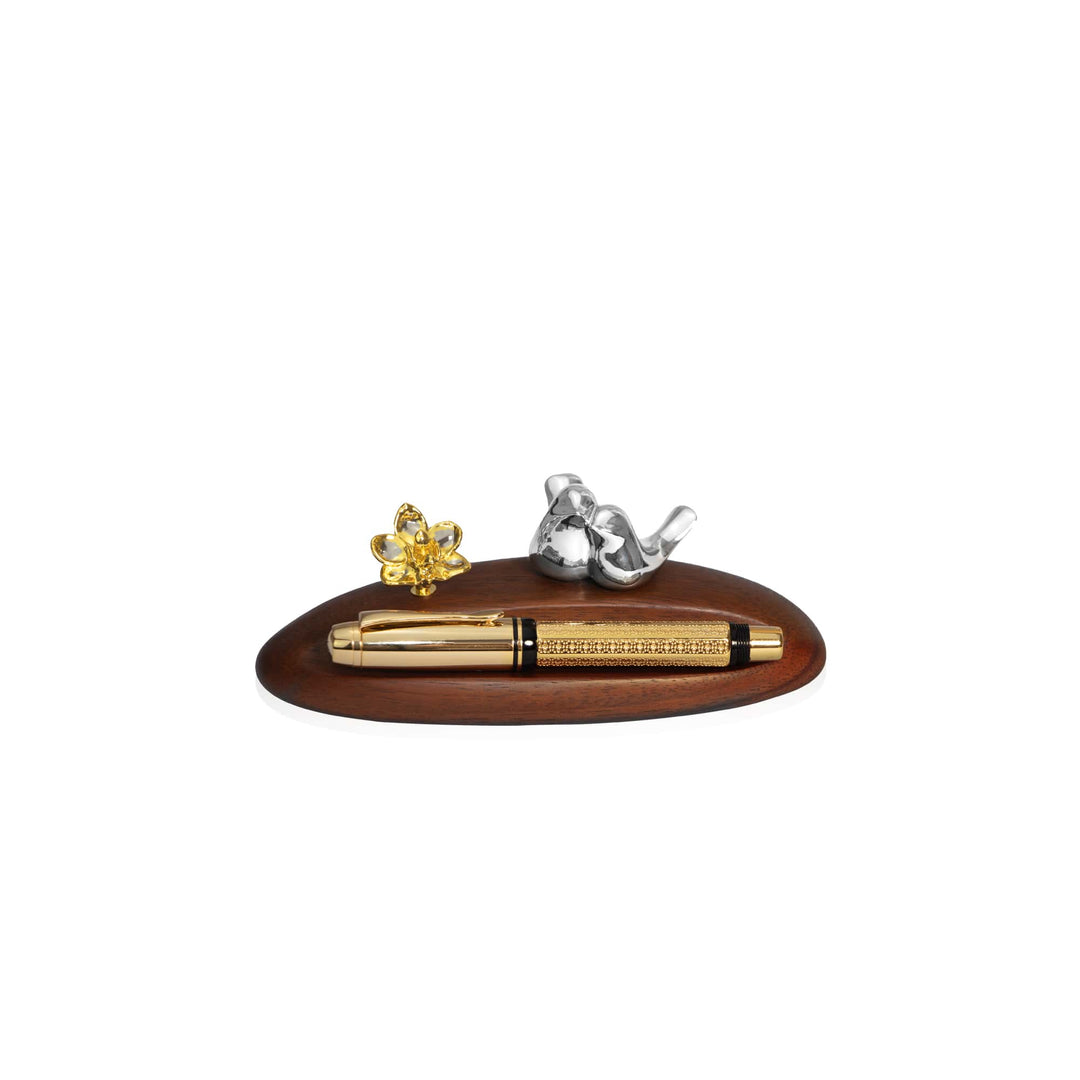 Risis Doritaenopsis Love Bird Pen Holder - A golden pen with detailed engravings lies on an oval wooden tray, flanked by a silver elephant figurine and a gold flower sculpture.