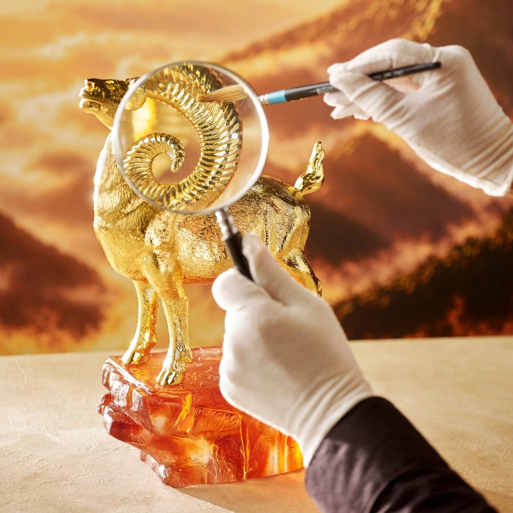 Golden argali figurine being examined near coiled horns on an amber base