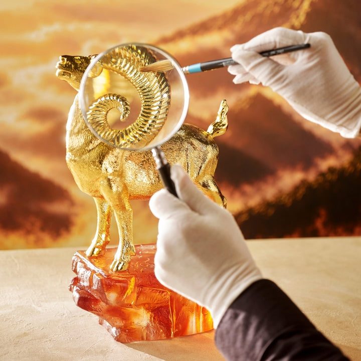 Golden argali figurine being examined near coiled horns on an amber base
