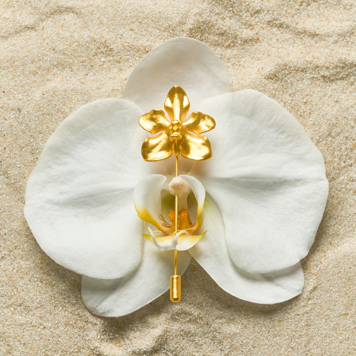 Risis Vanda Limbata Lapel Pin G - A golden orchid-shaped brooch pins together the petals of a white, real orchid flower, contrasting with its delicate texture and colors.