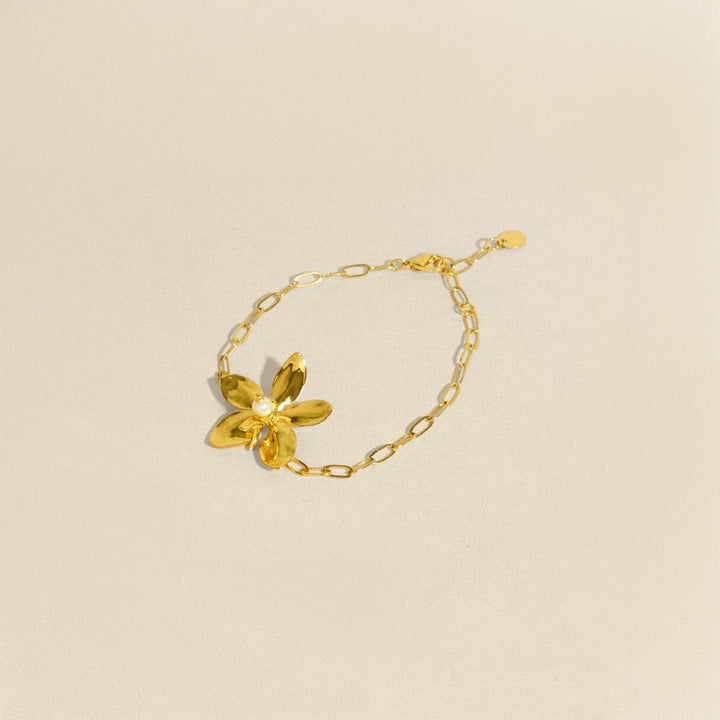 Risis Aeridovanda Blooms Bracelet - A golden bracelet features a single, five-petaled flower with a lustrous central gem, connected to a delicate chain. Its elegance is accentuated by the shiny finish.