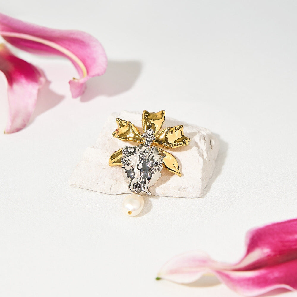 Risis Bapticidium Huwuduen Wasp Orchid Pearl Brooch - A brooch shaped like a flower rests on a white surface, featuring silver and gold tones, with a single pearl dangling below its petals.