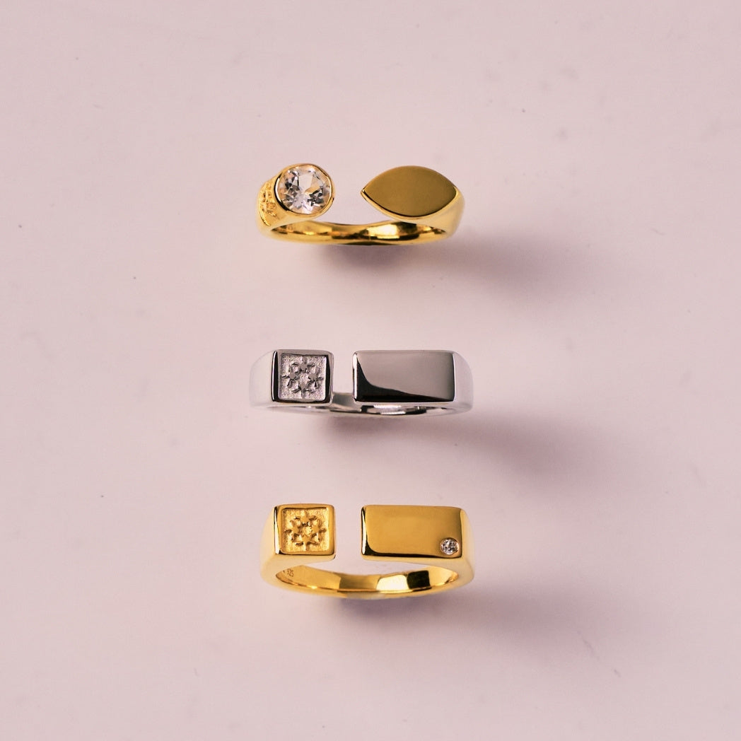 Three gold and silver open rings with geometric and gemstone details on a pink background - RISIS anniversary gifts