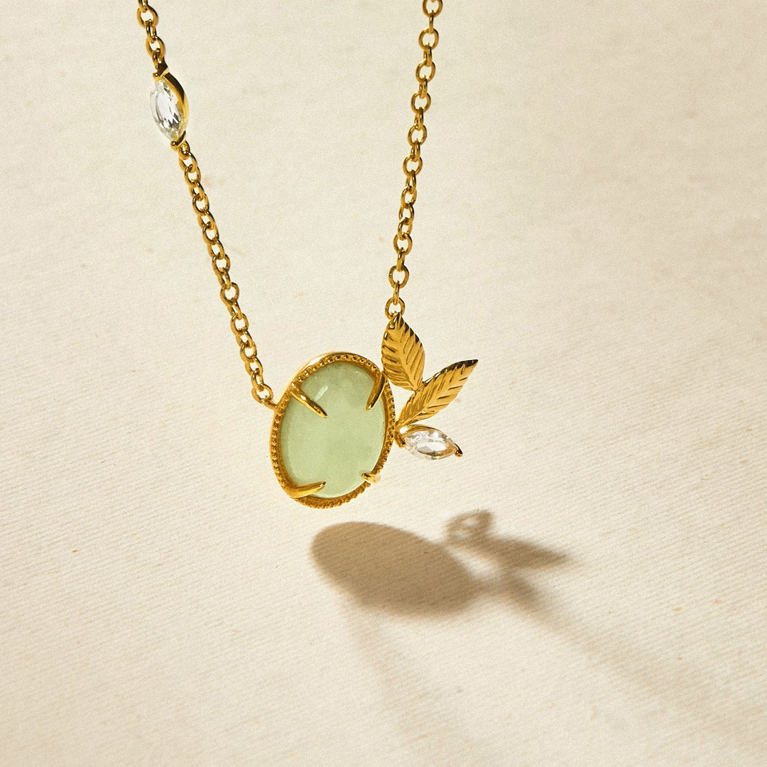 Risis Jadeite Prairie Necklace - A golden necklace with a pale green oval gemstone, accented with two gold leaves and a sparkling teardrop crystal.