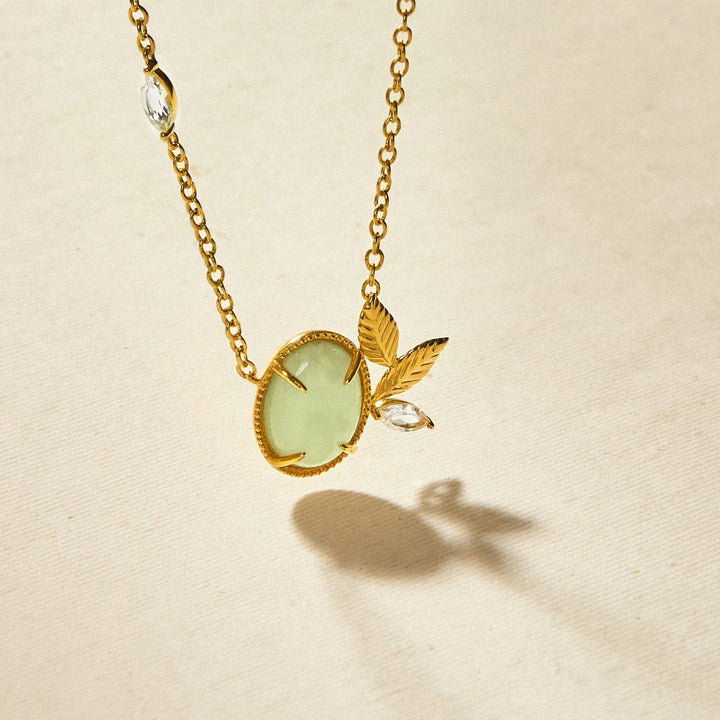 Risis Jadeite Prairie Necklace - A golden necklace with a pale green oval gemstone, accented with two gold leaves and a sparkling teardrop crystal.