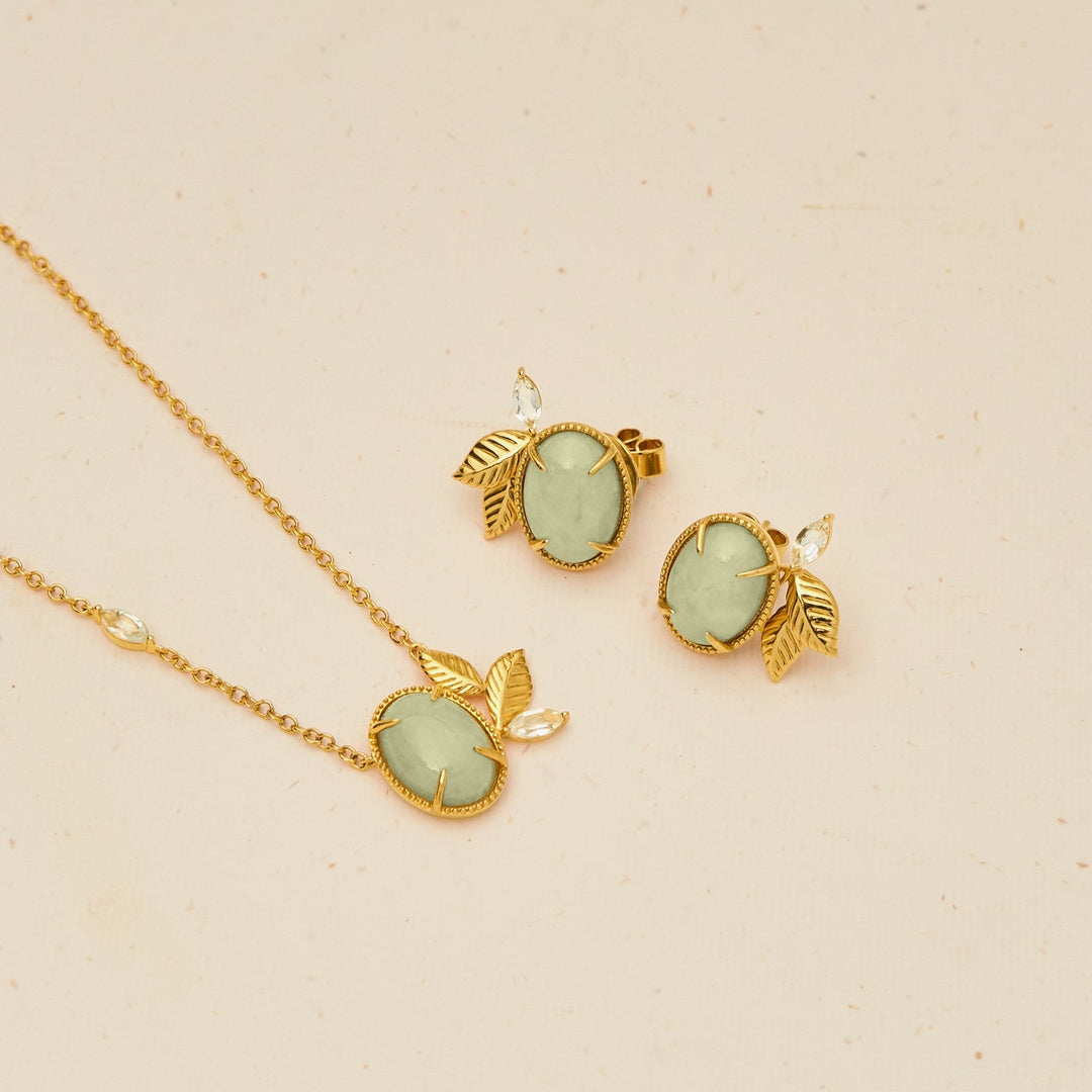 Risis Jadeite Prairie Necklace - A golden necklace and matching earrings with pale green gemstones, all adorned with leaf motifs, lay elegantly on a plain surface.