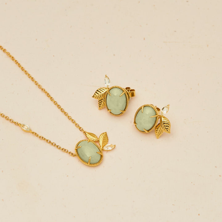 Risis Jadeite Prairie Necklace - A golden necklace and matching earrings with pale green gemstones, all adorned with leaf motifs, lay elegantly on a plain surface.