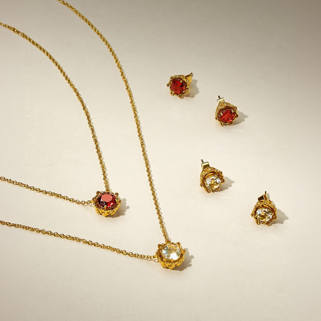 Risis Majestic Vanda Earrings With Red Garnet - Golden jewelry set with necklaces and matching earrings; some pieces feature prominent red gems, others clear stones, all set in intricately designed gold casings.