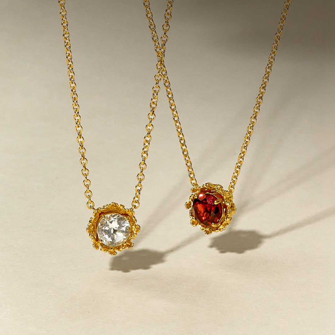 Risis Majestic Vanda Necklace With White Topaz - Two pendant necklaces with gold chains feature one clear crystal and one red gem, both encased in intricate golden settings.