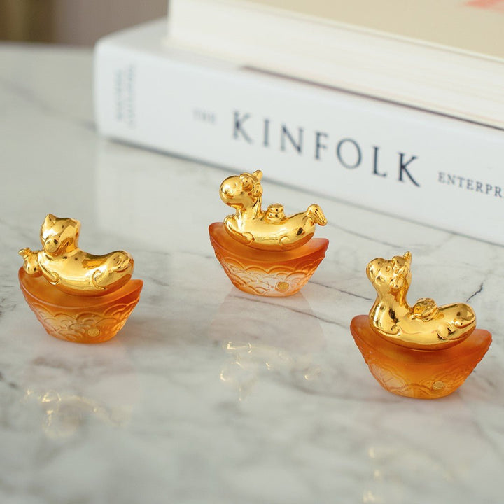 Risis Mini Celestial – Dog on Amber Liu Li - Three small, gold-and-orange figurines with ornate details and a glossy finish, displayed on a flat surface.