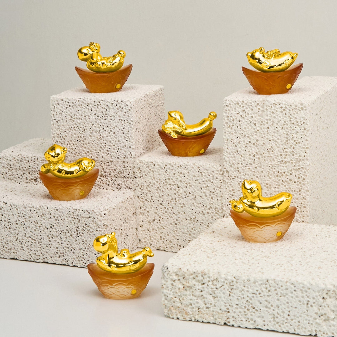 Risis Mini Celestial – Dog on Amber Liu Li - Six small, decorative gold-colored ingots on textured brown bases, arranged in two ascending rows on a multi-tiered white stand. The ingots have intricate designs and are glossy.