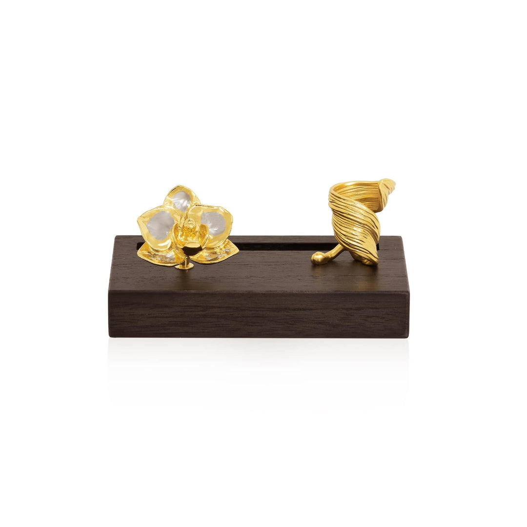 Risis Phalaenopsis Orchid Pen And Name Card Holder - A translucent flower-shaped object and a twisted, golden horn-like piece rest on a dark, wooden block, conveying a sense of artistic elegance.