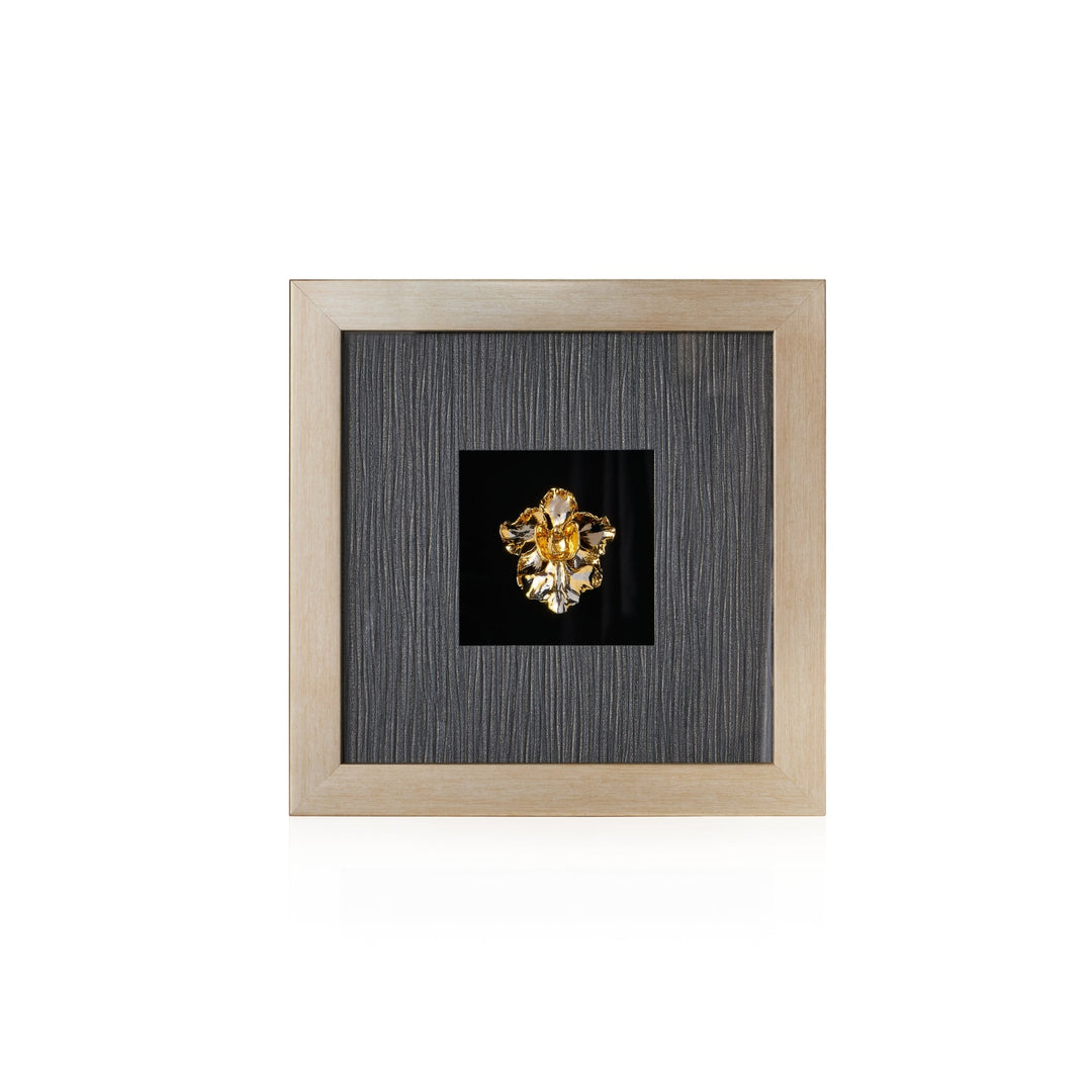 Risis Vanda Miss Joaquim Orchid Frame II - A golden floral brooch with intricate detailing and a central gemstone, mounted on a black backdrop and encased in a square, wooden frame.
