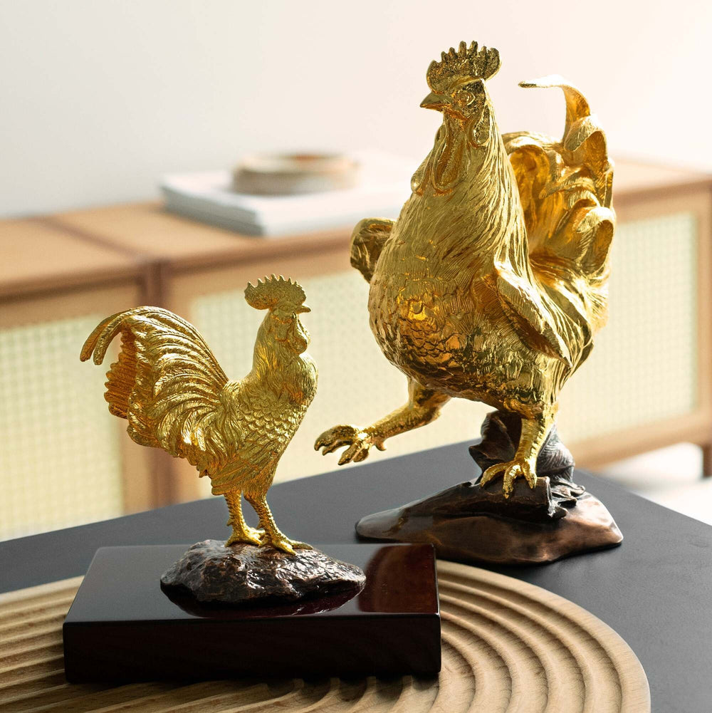 Risis Wisdom Rooster - Two golden rooster sculptures, one larger and prominently textured, standing on dark bases, exhibit elegance with their detailed feathers and poised stances.