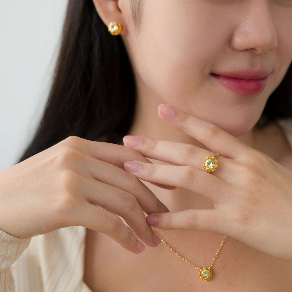 Risis Midori Earrings with Prasiolite - A person displays golden jewelry with prominent yellow gemstones. The matching earrings and ring are showcased on elegantly posed hands, enhancing the pieces' visual allure.