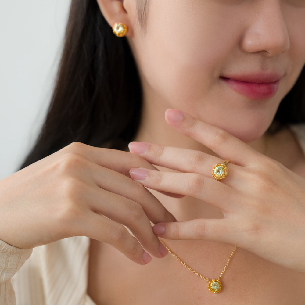 Risis Midori Necklace With Prasiolite - A person is wearing gold jewelry with prominent golden-yellow gemstones, including earrings, a ring on their finger, and a pendant on a delicate chain necklace.