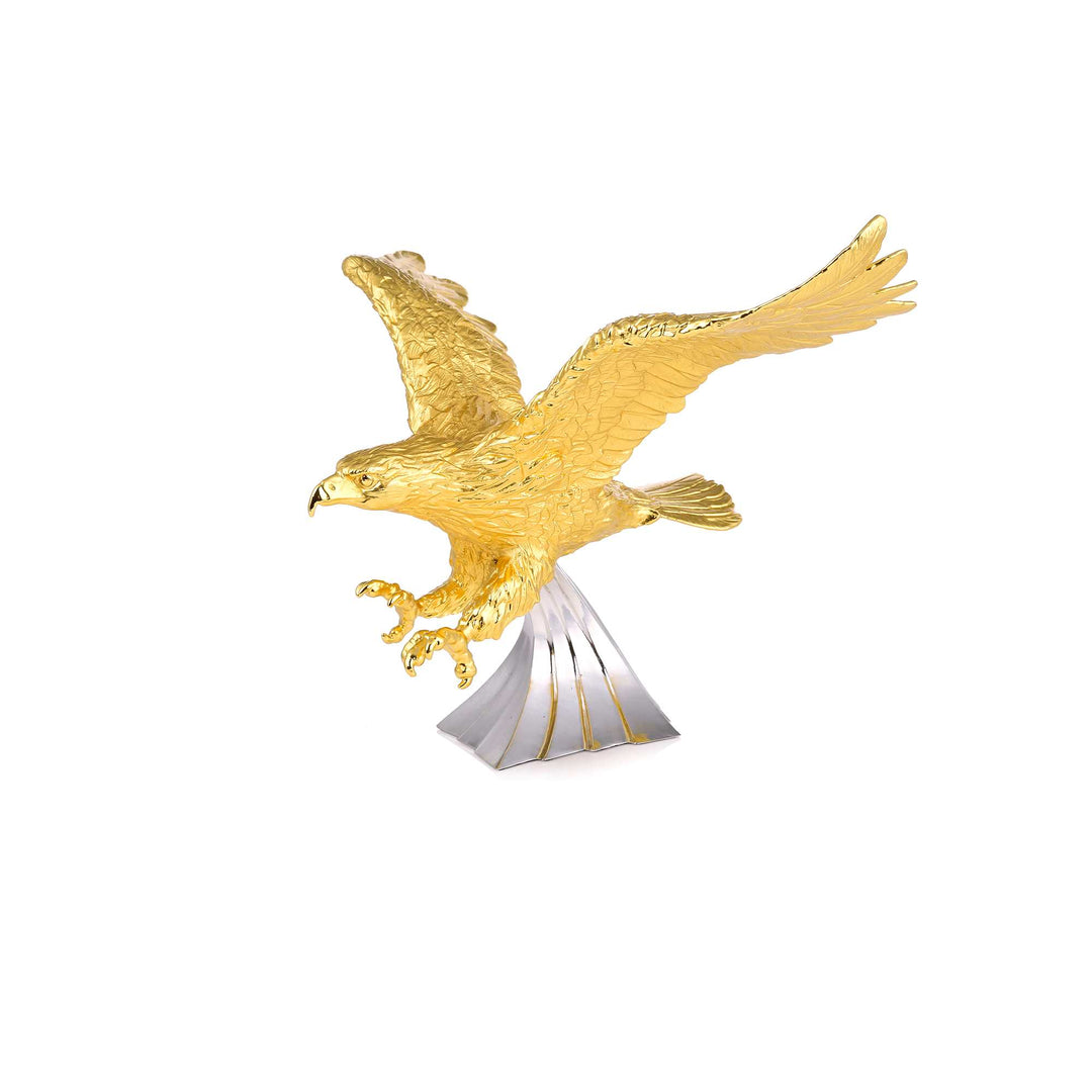 Risis Northern Prince Eagle - A golden sculpture of an eagle in mid-flight, with detailed feathers and outstretched talons, mounted on a simple silver-toned pedestal with subtle accents.