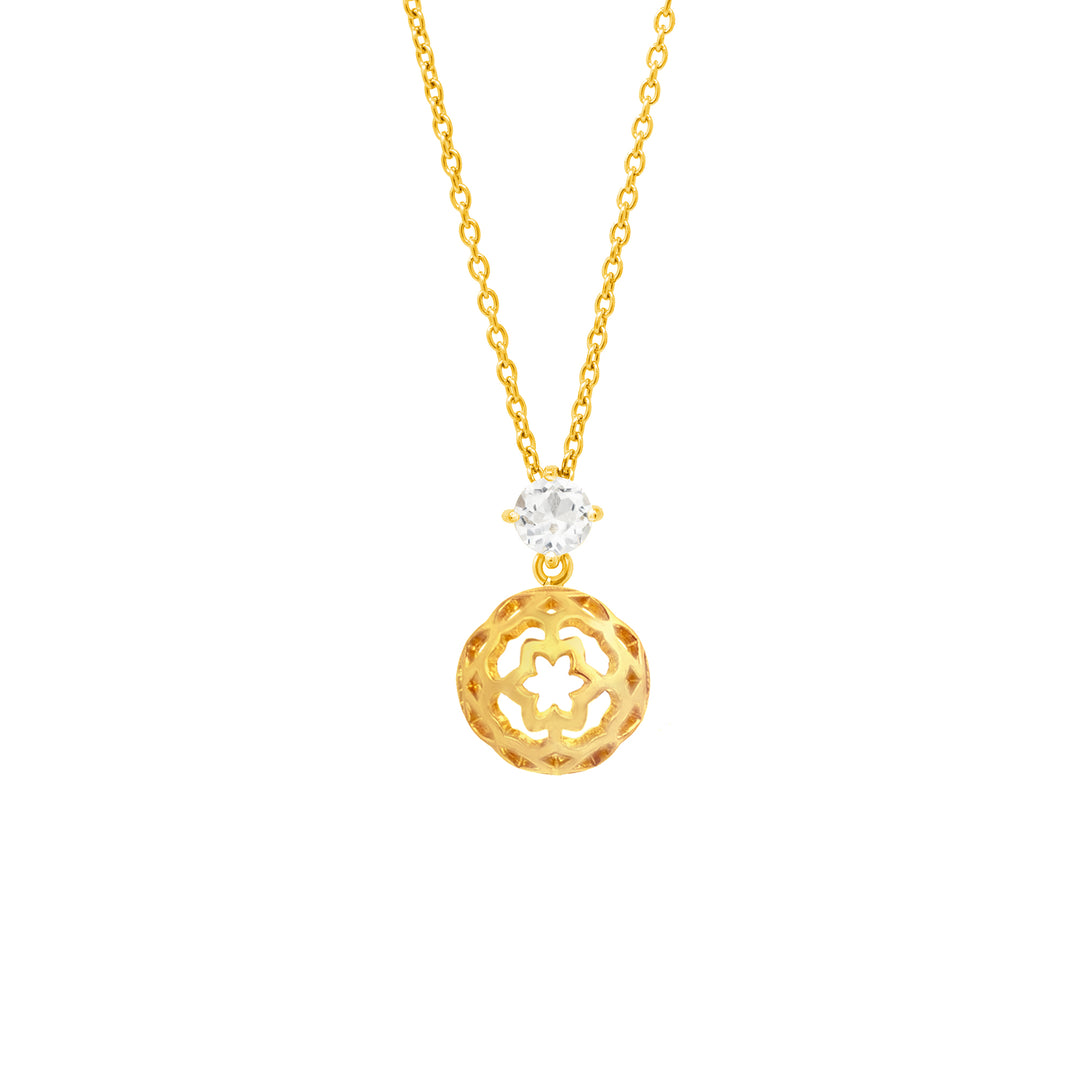 Risis - A golden pendant with intricate cut-out patterns hangs from a delicate chain, accented by a sparkling gemstone above it. The colors are warm and the craftsmanship detailed.