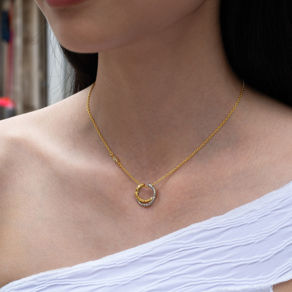 Risis Bamboo Twist Necklace with White Sapphires - A golden necklace with a sparkling, horseshoe-shaped pendant adorns a person's neck, exhibiting elegance and simplicity.