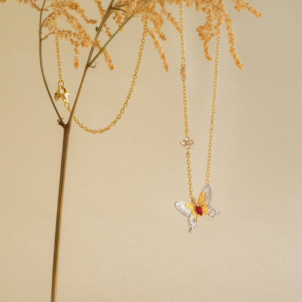 Risis Botanique Butterfly Necklace - Two metallic, leaf-shaped dishes with a glossy finish, one adorned with a golden bird and flower, accompanied by two smaller golden flowers nearby.