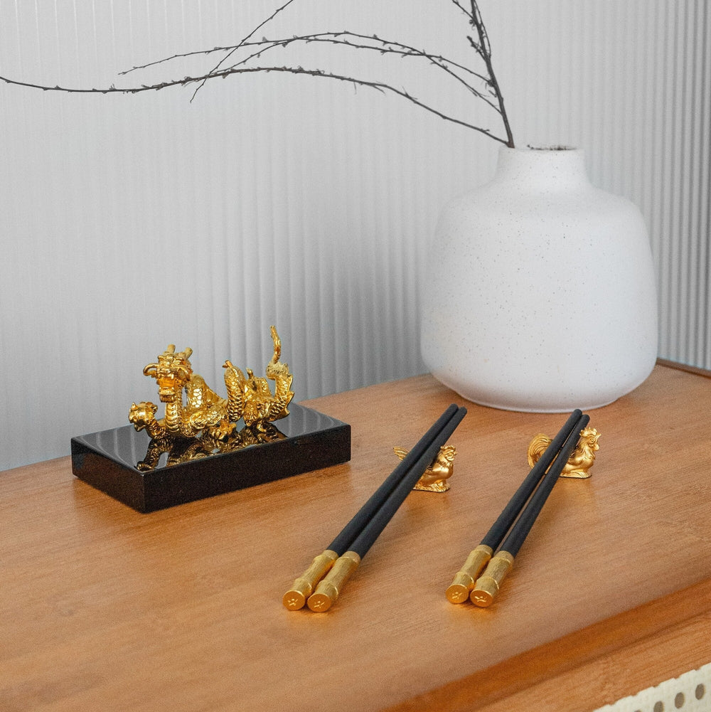 Risis Chopsticks with Rooster and Hen Rests - Golden figurines are staged alongside ornate chopsticks with gold accents, displayed on a wooden surface, suggesting an elegant, decorative setting.