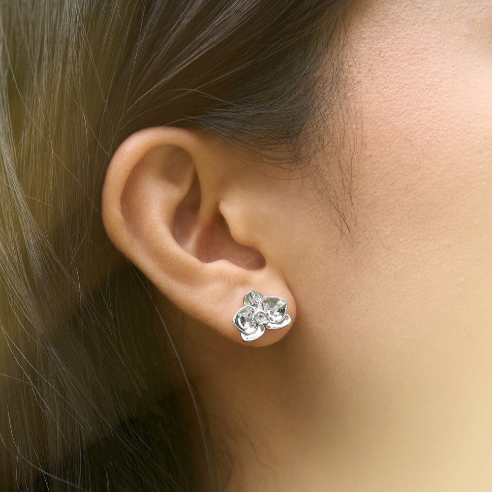 Risis Dainty Phalaenopsis Earrings - A silver floral earring with transparent gem petals adorns a person's earlobe, featuring a polished finish that captures the light and showcases intricate craftsmanship.