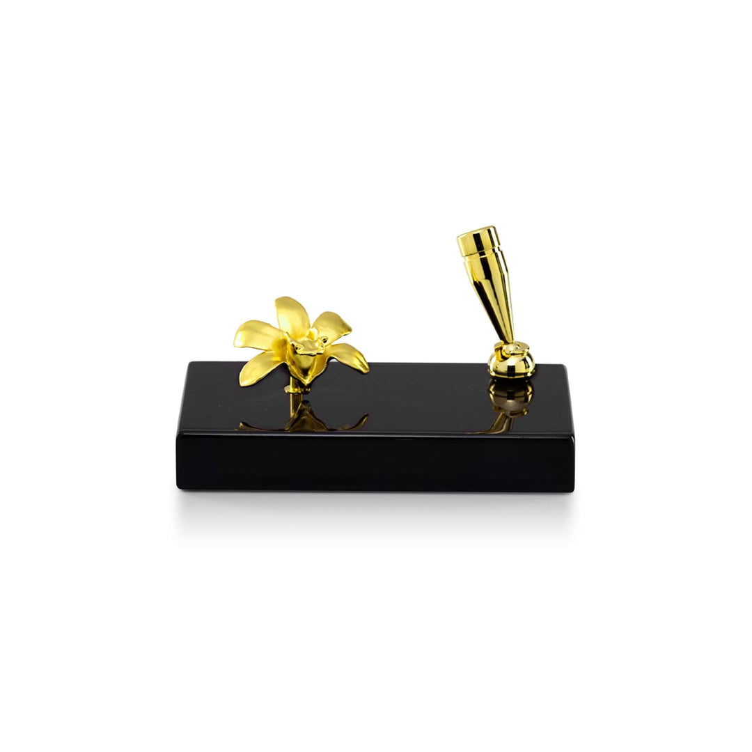 Risis Dendrobium Orchid Pen Holder (L1) - A golden flower and pen rest on a sleek, black rectangular base, their metallic sheen contrasting with the dark, reflective surface.
