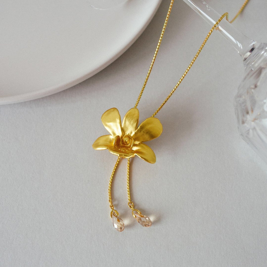 Risis Dendrobium Thong Chai Orchid Slider Necklace with Crystal Tailends (G) - A golden necklace with a flower pendant; the flower has five petals and two dangling chains with transparent bead accents.