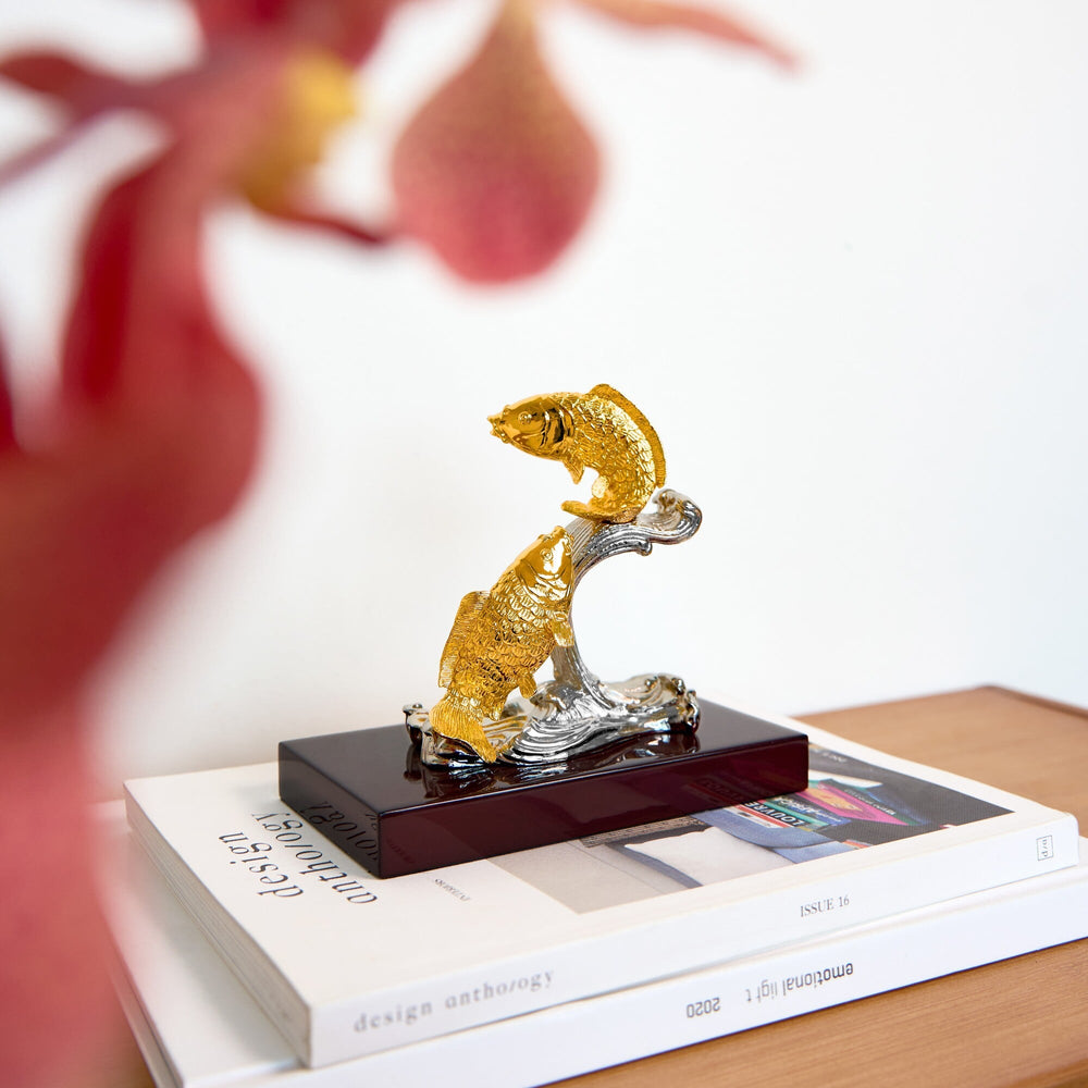 Risis Double Carps on Wave with Flat Base - A golden fish ornament with detailed textures leaps from silver waves, displayed atop a stack of books.