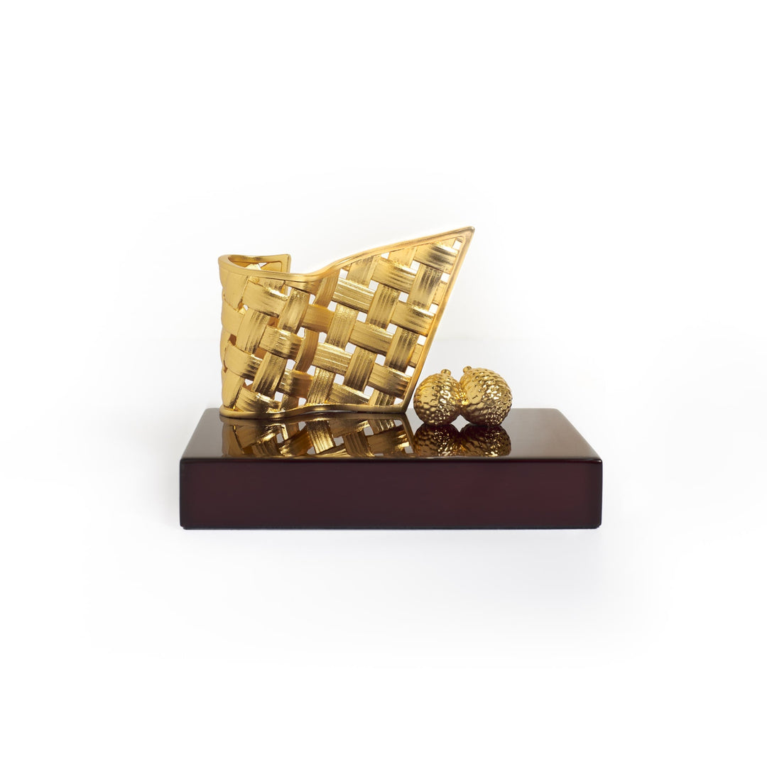 Risis Entwined Rattan Pen and Name Card Holder - A golden, textured clutch bag with a geometric pattern displayed beside a spherical, studded ornament, both resting on a dark, glossy base.