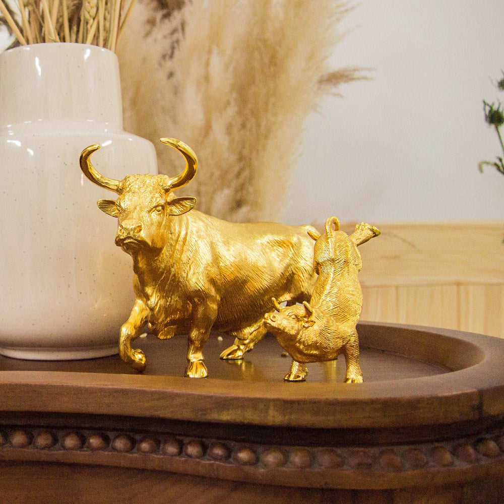 Risis Legend of XII - Ox - A golden sculpture depicts a bull with horns followed by a calf, showcasing fine textures and a shiny finish, displaying on a wooden surface.