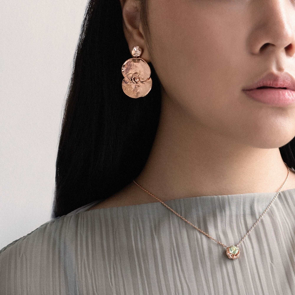 Risis Midori Necklace with Prasiolite (RG) - A pair of rose-gold earrings with large yellow-green gemstones, complemented by a matching ring, adorn a person's ear and hand, highlighting the shimmering, vibrant colors of the jewelry.