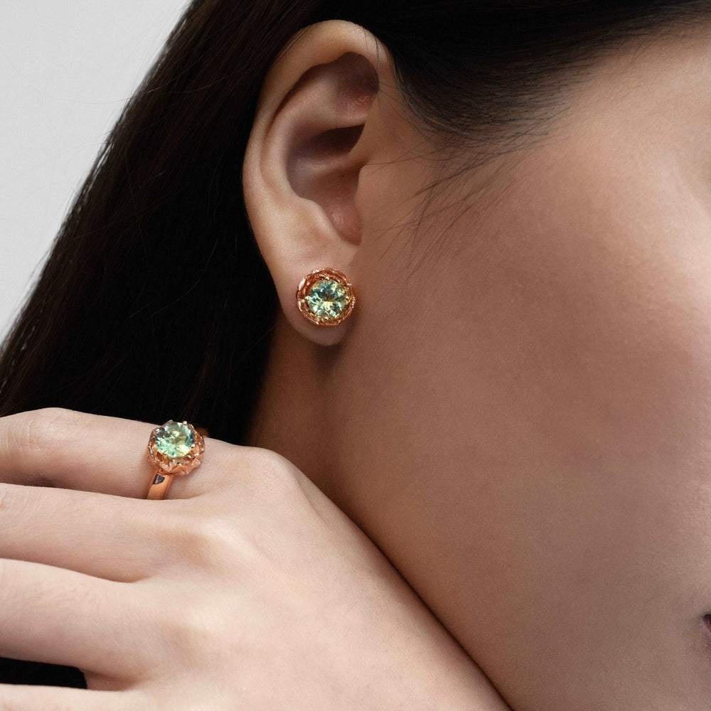 Risis Midori Ring with Prasiolite (RG) - A woman is wearing rose gold, textured earrings and a delicate necklace with a small, sparkling heart-shaped pendant. The jewelry exudes sophistication and elegance.