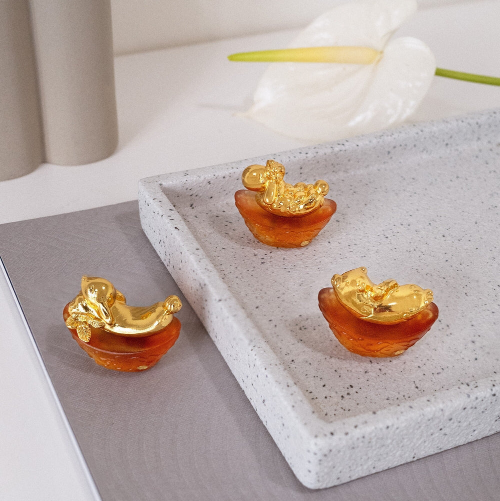 Risis Mini Celestial – Pig on Amber Liu Li - Three golden figurines resembling mythological creatures, with intricate details, are perched within translucent amber bowls on a textured gray surface.