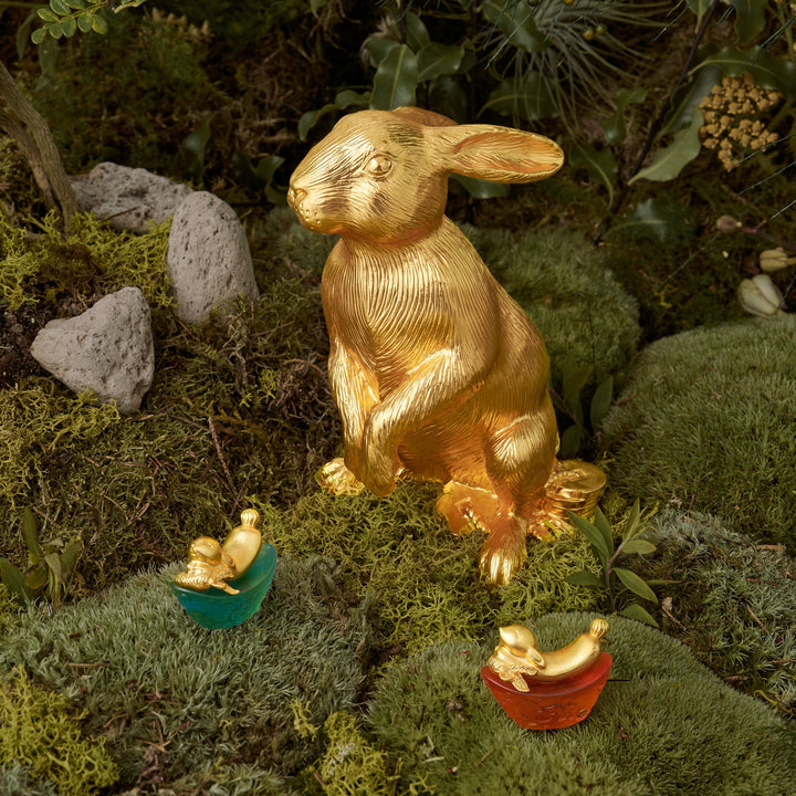 Risis Mini Celestial – Rabbit on Green Liu Li - A golden rabbit with a textured surface is pictured next to two smaller figurines, one bird and one bunny, nestled in colorful egg-shaped containers.