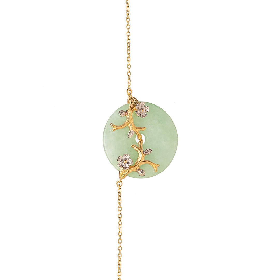 Risis Nature's Jade Long Necklace with White Topaz (L) - A gold pendant features a delicate vine with sparkling flowers set against a pale green circular backdrop, suspended from a fine gold chain.