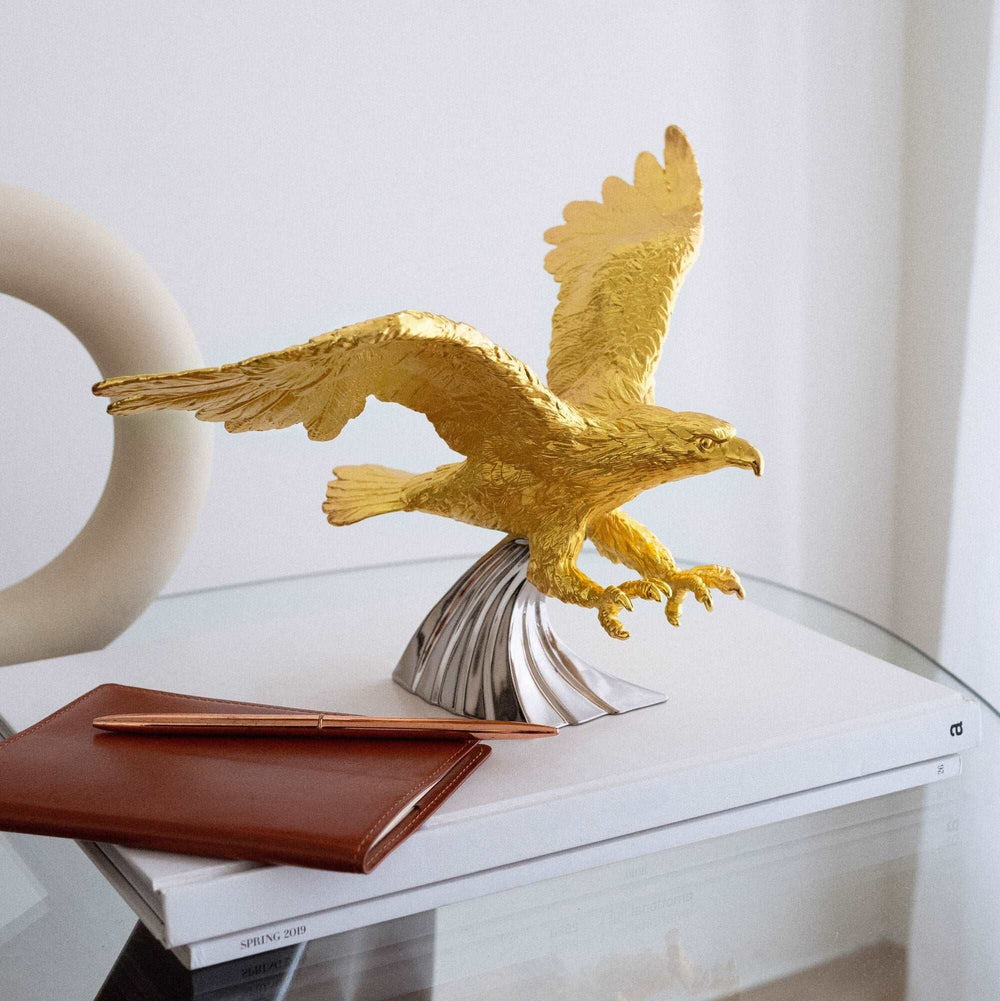 Risis Northern Prince Eagle - A golden eagle sculpture poised for flight with intricate feather textures, mounted on a polished silver base, sits atop a glass surface.