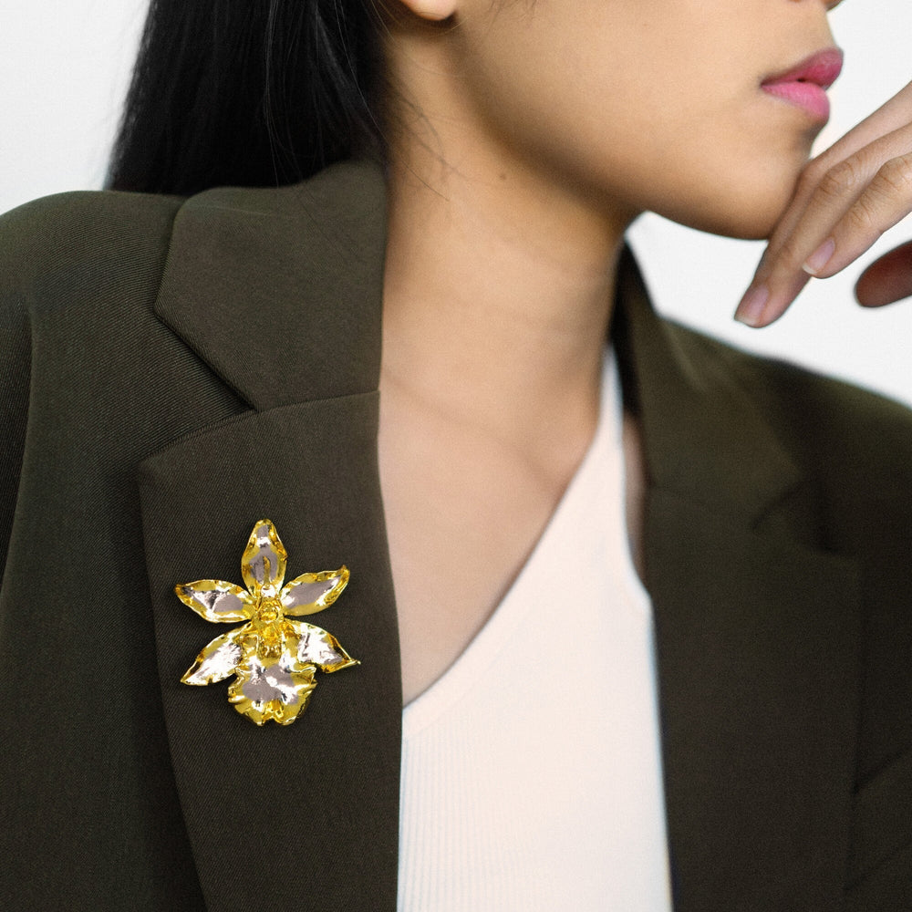Risis Oncidium Wildcat Orchid Brooch/Pendant (PG) - A person is wearing a gold-toned floral brooch with yellow gem-like accents on the lapel of a dark green blazer.