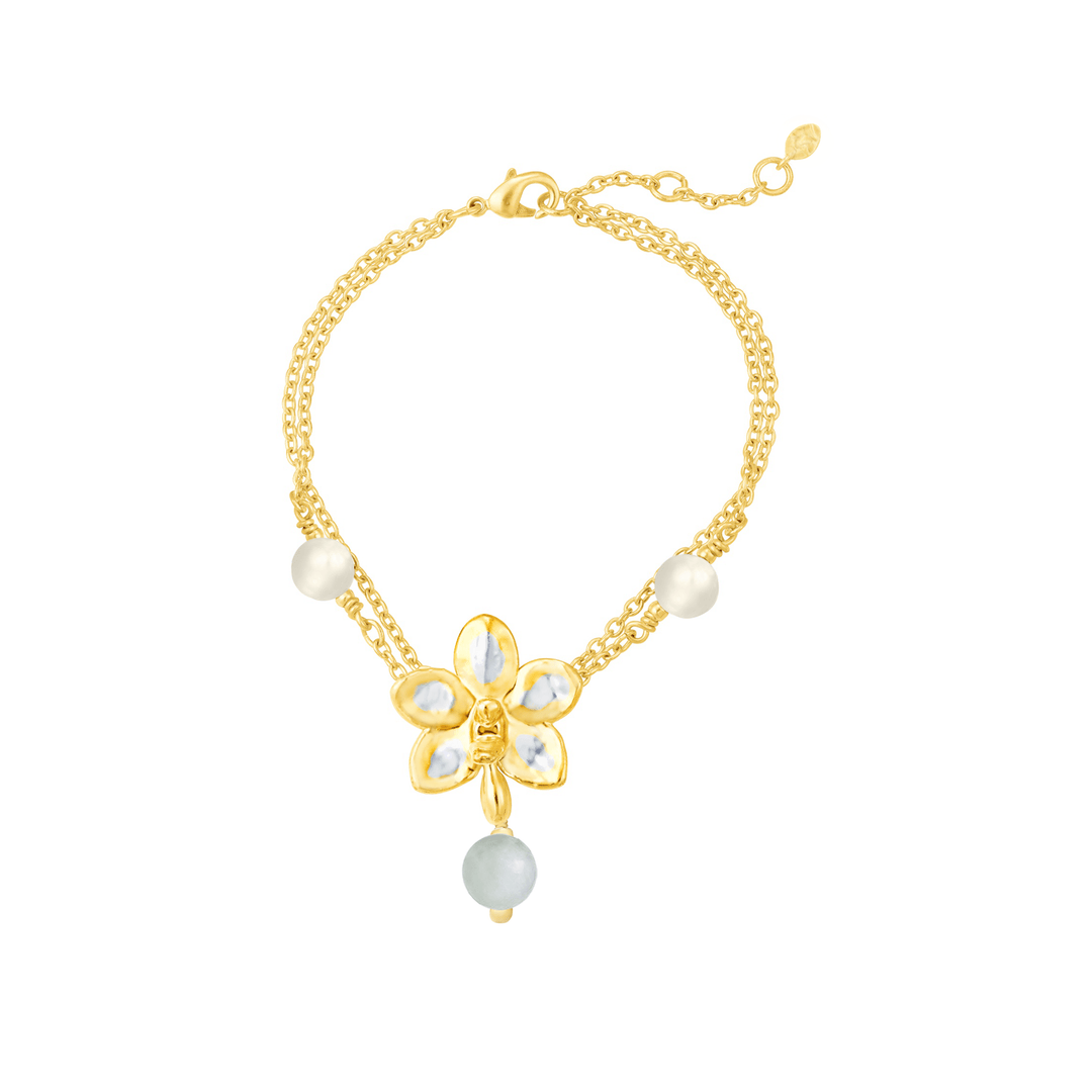 Risis Orchid Meadows Bracelet with Jade and Pearl - A golden bracelet featuring a central flower charm with white and yellow accents, complemented by pearls and a delicate blue bead dangling below.