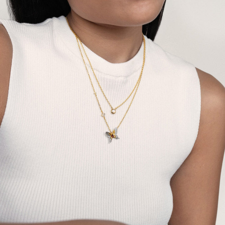 Risis Peranakan Jewel Necklace with Moonstone - A person wears layered necklaces; one with a simple pearl and another featuring a sparkling, multicolored, bee-shaped pendant.