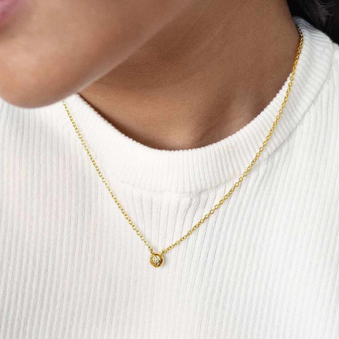 Risis Peranakan Jewel Necklace with Moonstone - A delicate gold necklace with a small, spherical pendant, worn against a plain white garment. The pendant gleams with a polished finish, conveying simplicity and elegance.