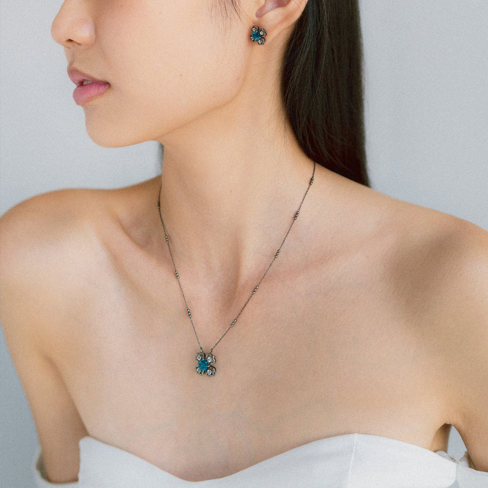 Risis Peranakan Kebaya Earrings (BRH) with London Blue Topaz - A person is wearing a delicate, dark-toned necklace with a floral pendant and matching floral earrings, both featuring turquoise accents.