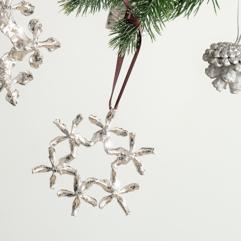 Risis Renantanda Sawadi Orchid Ornament (RH) - A silver snowflake ornament, reflective and textured, dangles by a maroon ribbon, resembling a delicate icy crystal.