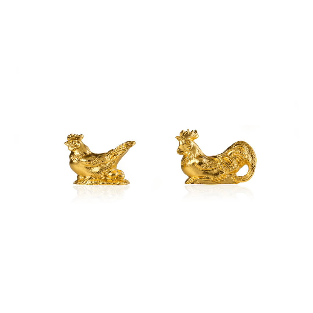 Risis Rooster and Hen Chopstick Rests - Two golden rooster figurines, intricately detailed and polished, with prominent plumage and crests, reflecting light on a plain surface.