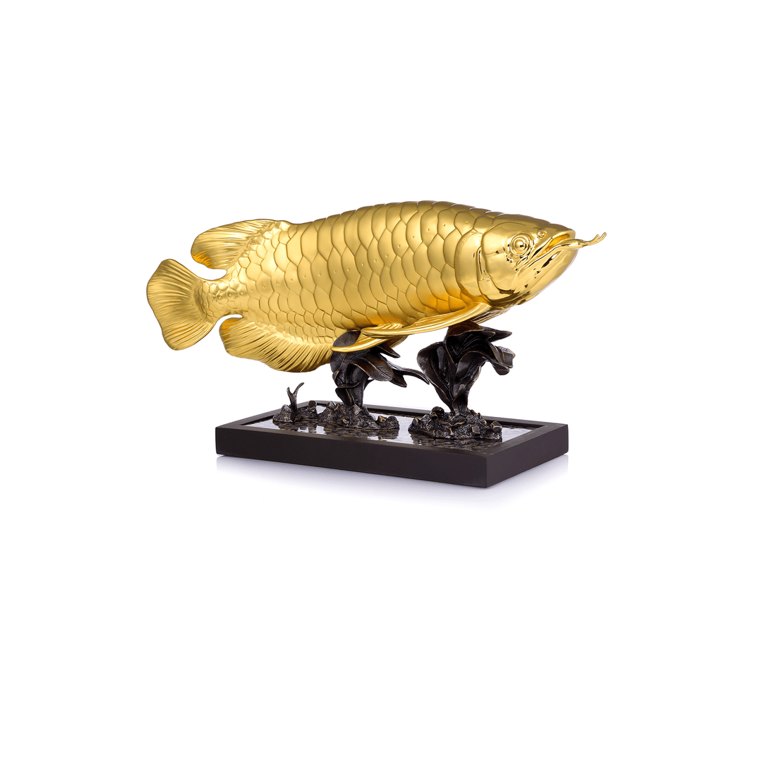 Risis Supreme Arowana - A golden fish sculpture with detailed scales is perched atop a dark, ornate base resembling vegetation, creating a contrast of colors and textures.