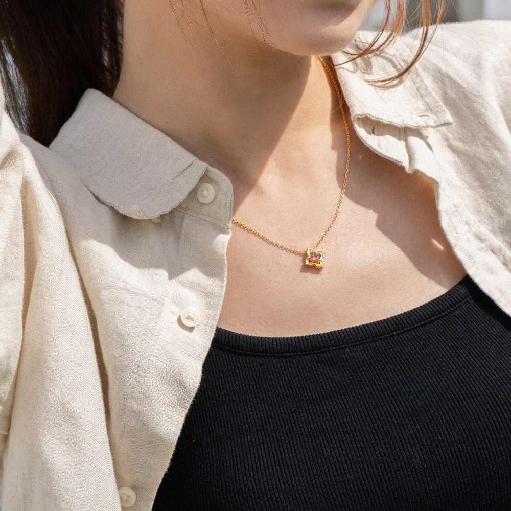 Risis Timeless Peranakan Necklace With Pink Tourmaline - A delicate gold necklace with a small, ornate pendant featuring a vivid purple gem, gracefully adorns the person's neck.
