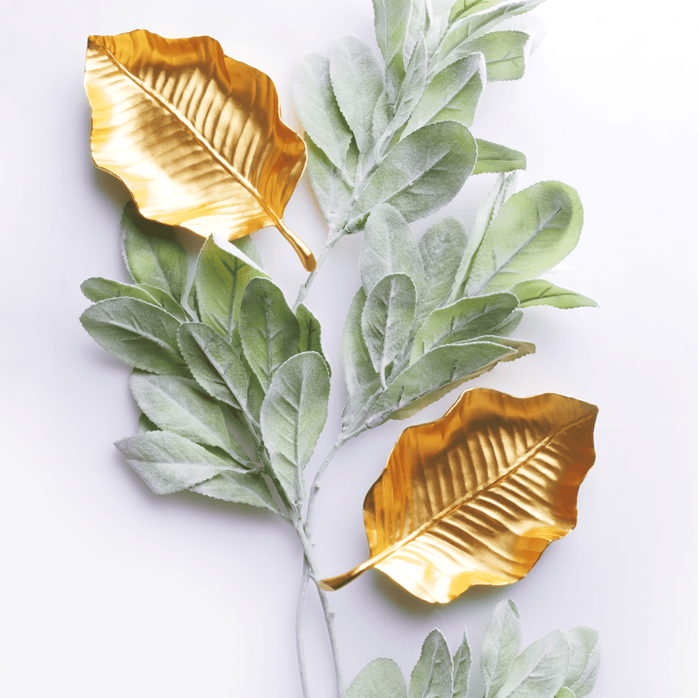 Risis Tropical Leaf Tray - Two golden metallic leaves are accompanied by branches of delicate, velvety green leaves, contrasting textures and colors in an artistic arrangement.