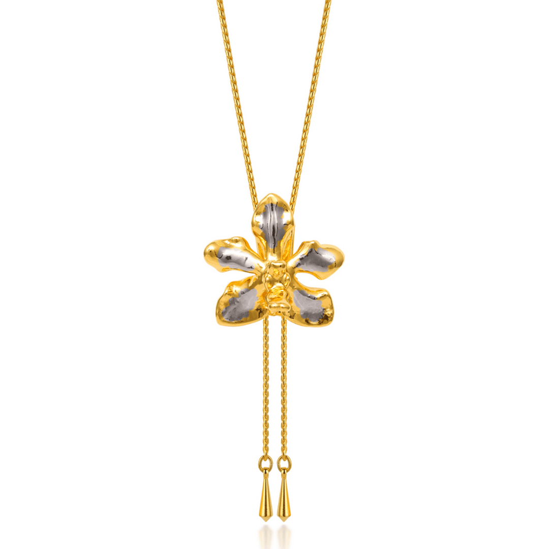 Risis Vanda Limbata Orchid Slider Necklace (PG) - A shiny gold pendant in the shape of a four-leaf clover with a glossy finish hangs from a delicate chain, accompanied by two tasseled strands.